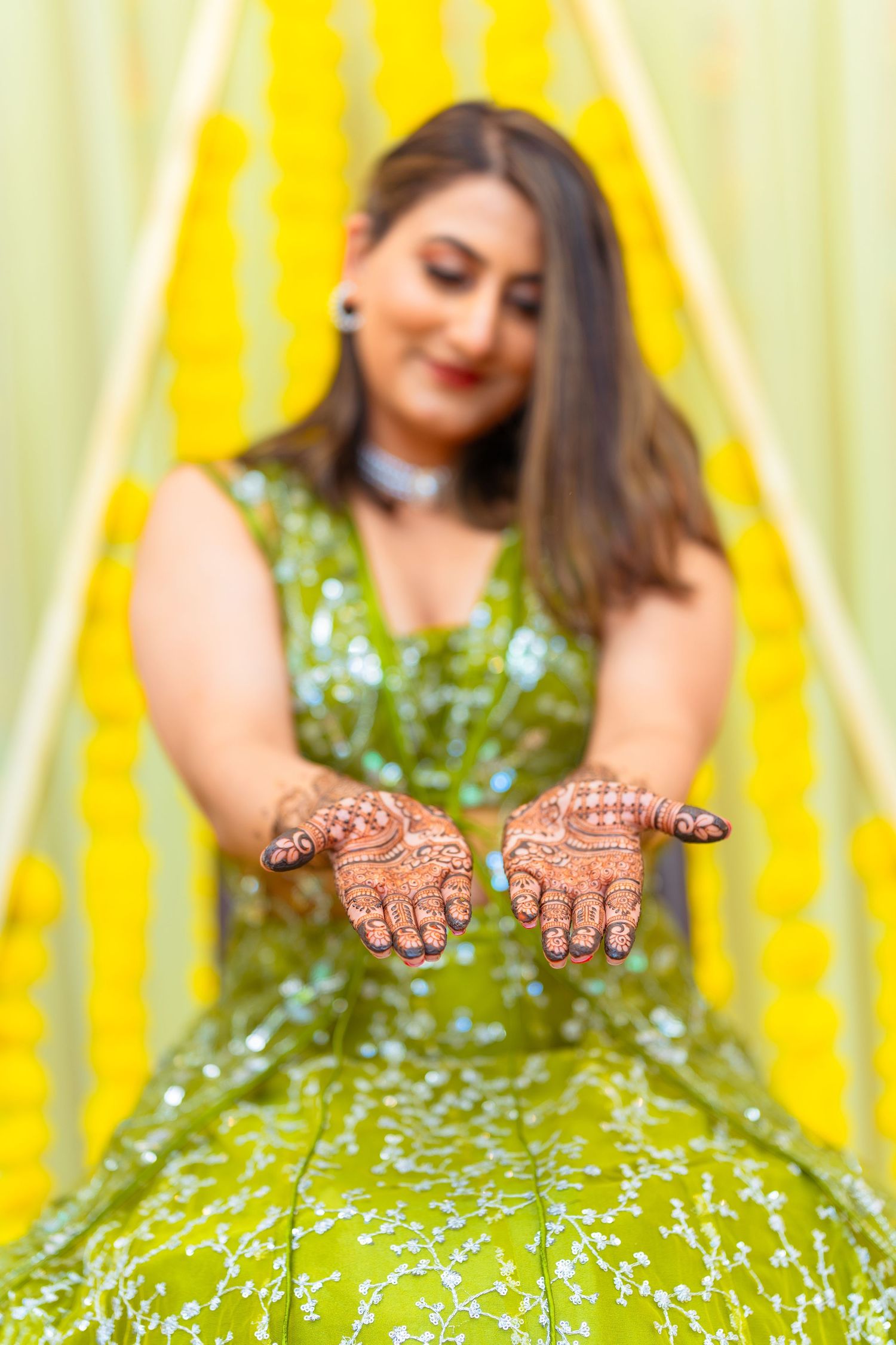 Detailed view of henna patterns on palms with green lehenga in foreground.