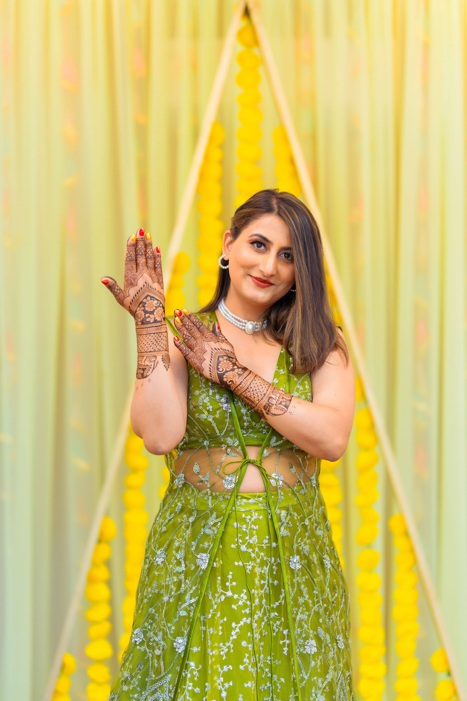 Woman poses showing traditional henna designs against yellow triangle backdrop.