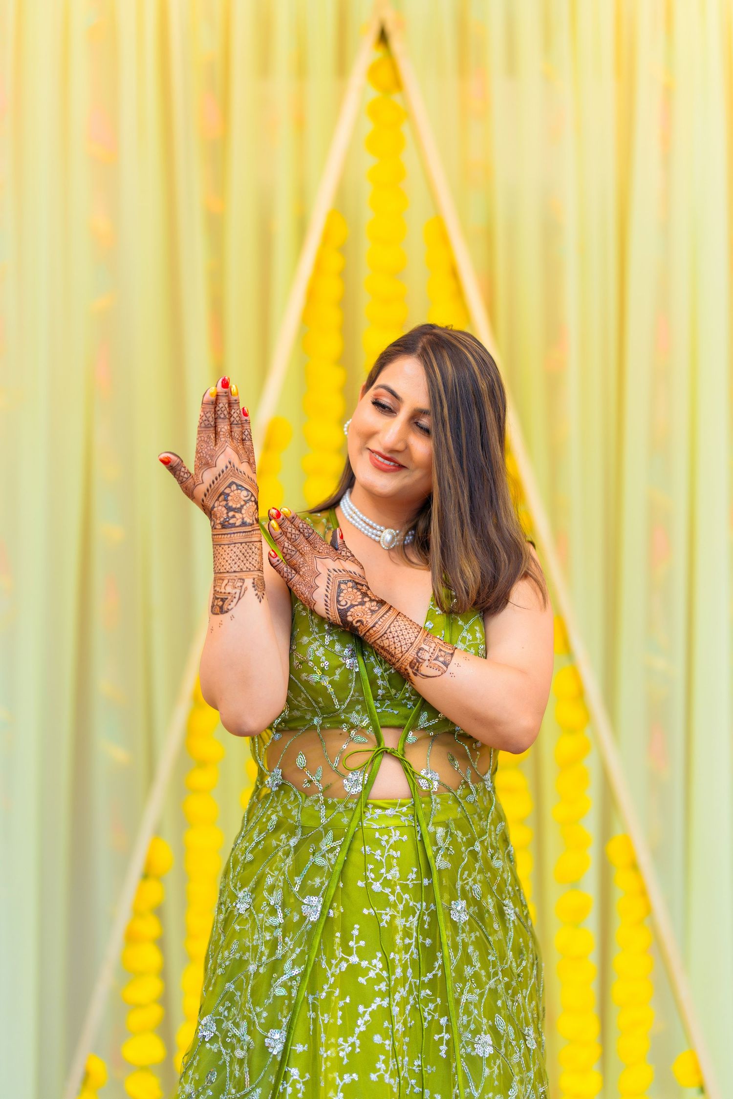 Beautiful green lehenga with intricate henna designs shown against yellow backdrop during wedding celebrations.