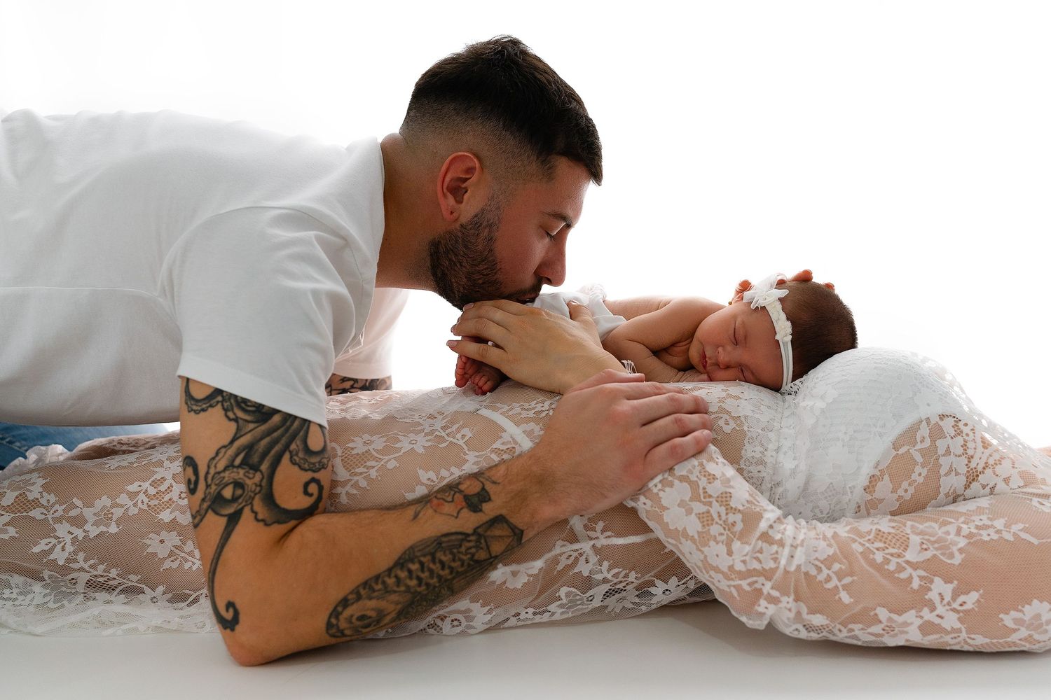 An intimate maternity photoshoot featuring a tender moment between couple on white backdrop.