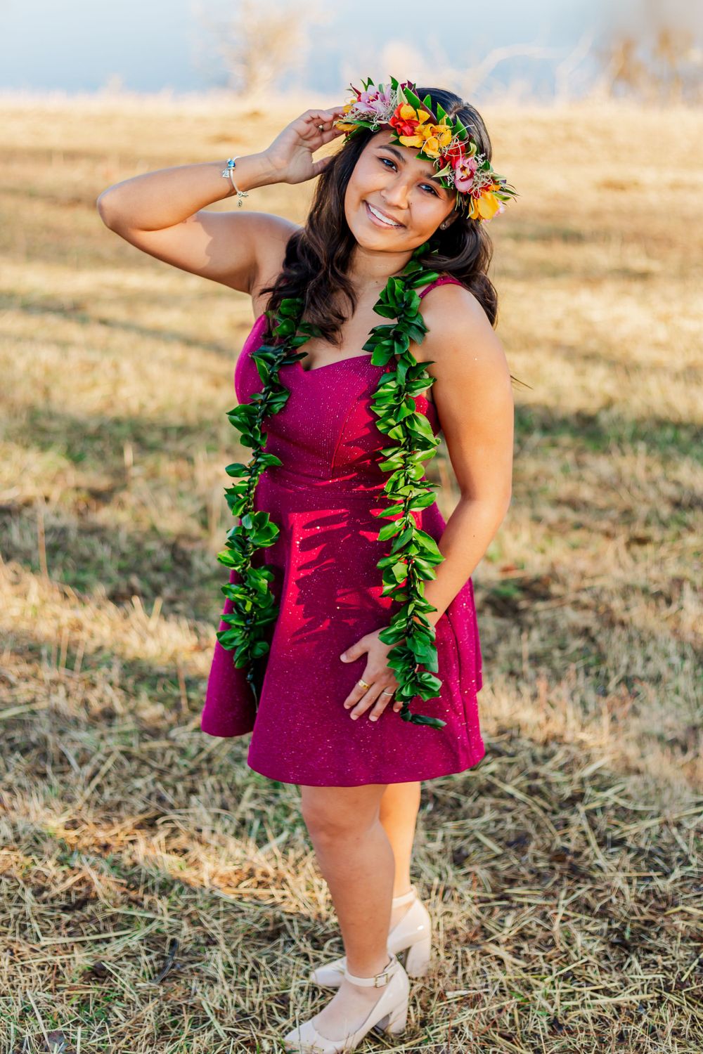 Joyful outdoor portrait in magenta dress with tropical flower crown and green leaf garland.
