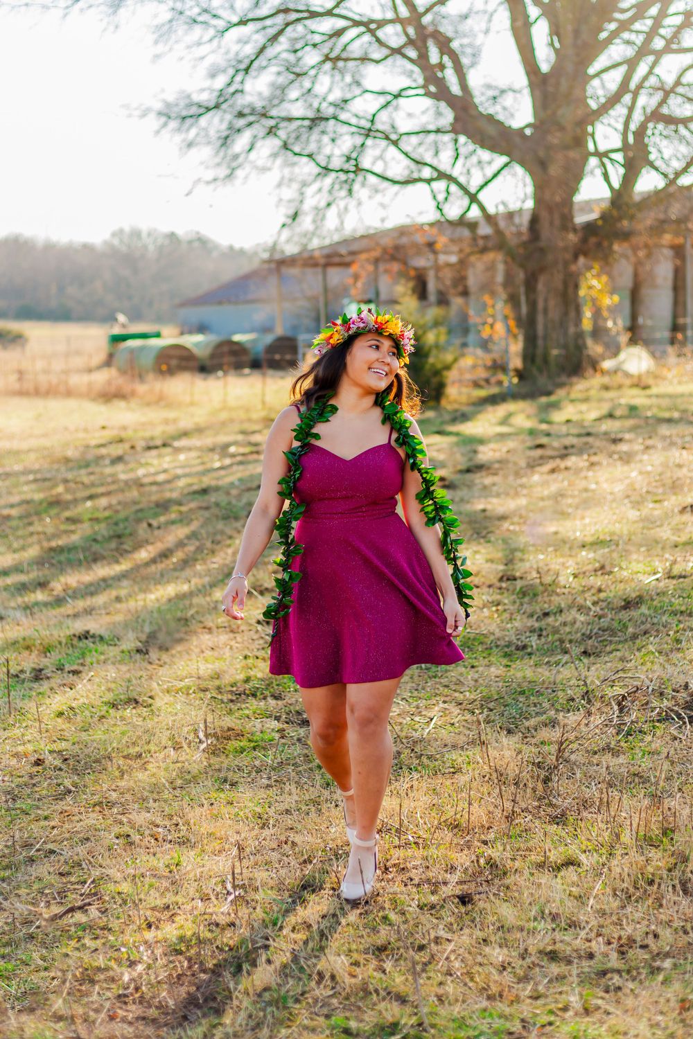 Figure in flowing magenta dress with floral accessories strolls through sunny field.