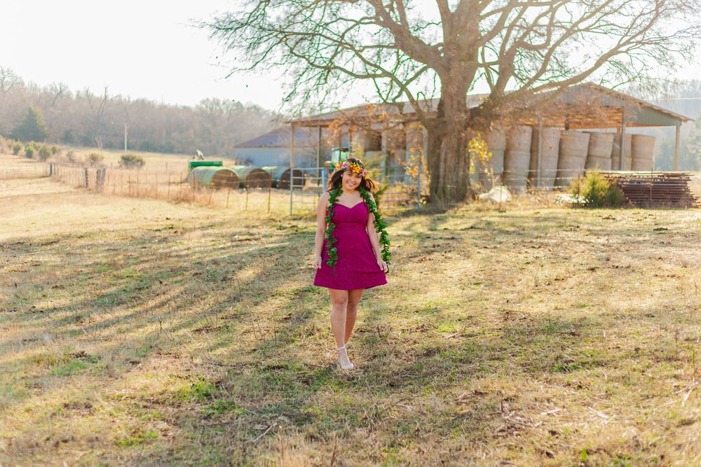 Person in magenta dress and floral accessories walks through rural countryside setting.