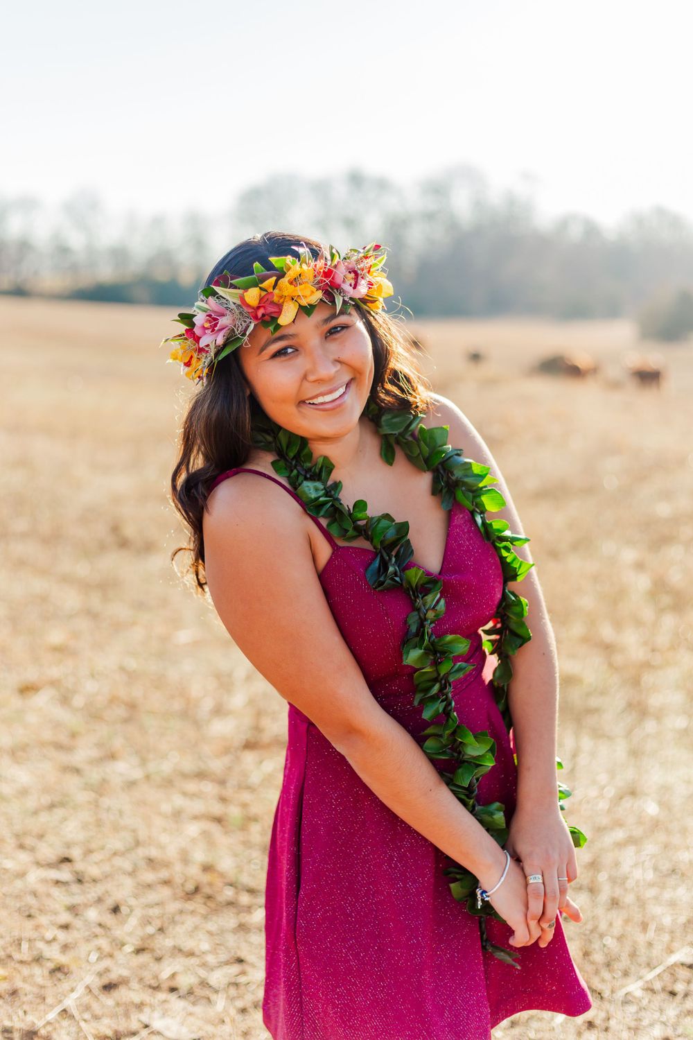 Outdoor portrait with bright magenta dress, flower crown and green lei against golden field.