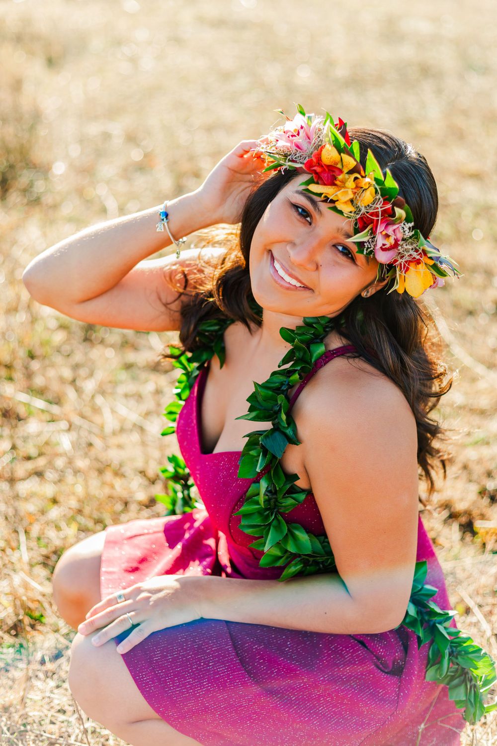 Portrait in a sunny field wearing magenta dress, floral crown and green leaf lei.