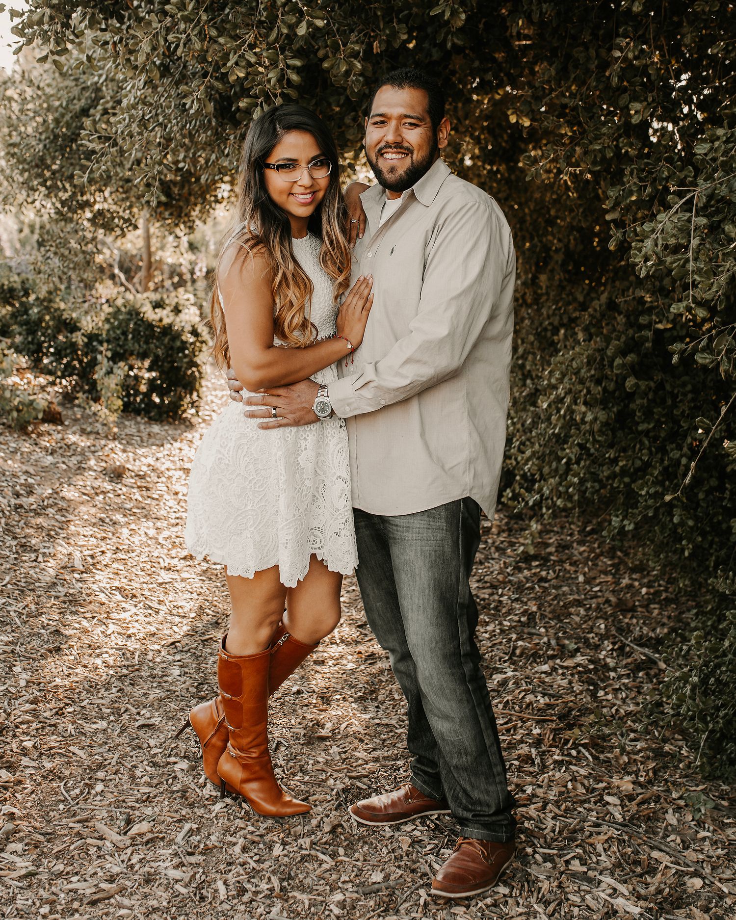 Couple in casual attire shares romantic moment on leaf-covered ground in forest setting.
