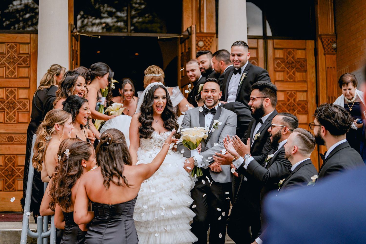 action shot of a bride and groom making their grand exit from the church wedding venue while family and friends cheer and throw flowers