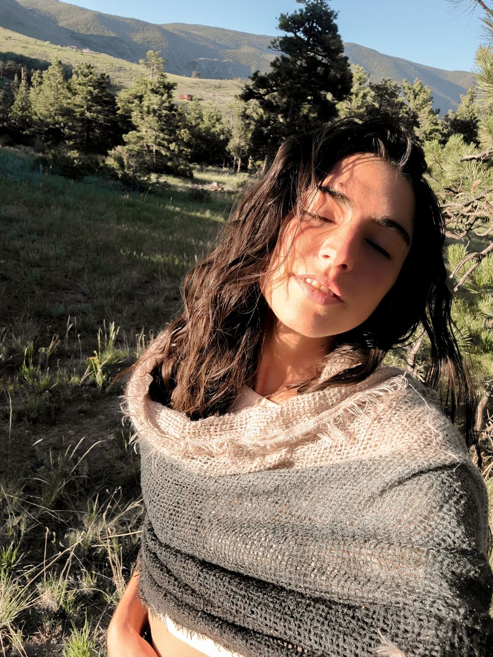 Outdoor portrait against mountain landscape with person wearing gray knit wrap.