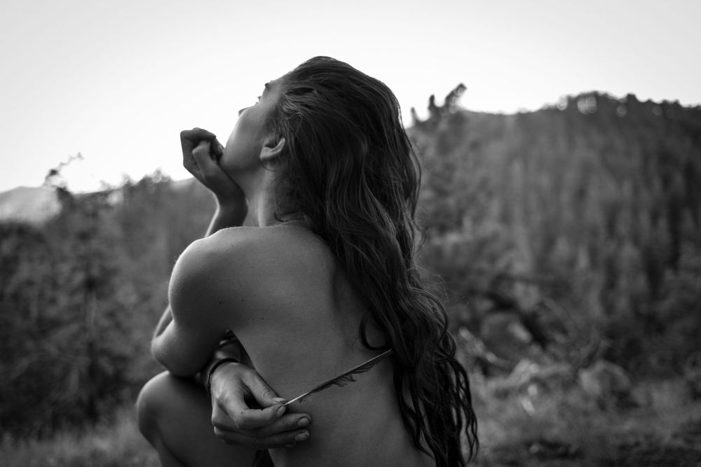 Artistic black and white portrait of person with flowing hair against mountain silhouette.