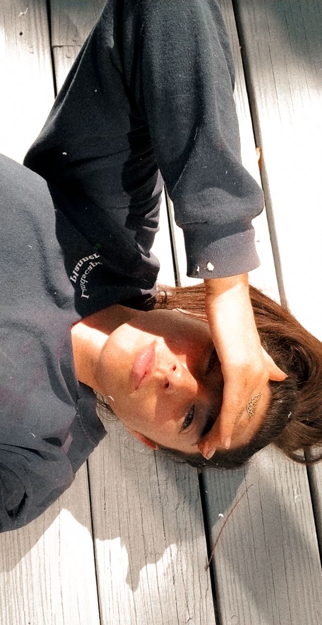 Person in dark hoodie lying on wooden deck in sunlit setting.