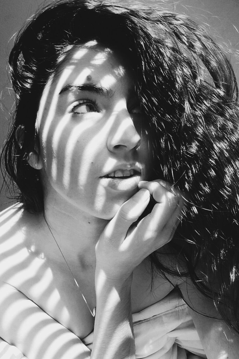 Black and white portrait with dramatic venetian blind shadows creating striped lighting effect.