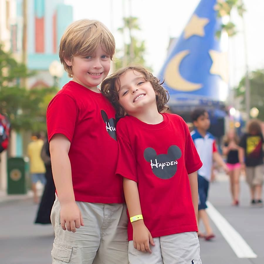 Two children in matching red t-shirts sharing a happy moment at a theme park.