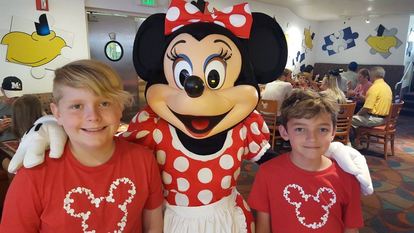 Visitors in matching Mickey Mouse themed shirts meet Minnie Mouse at Disney character dining restaurant.