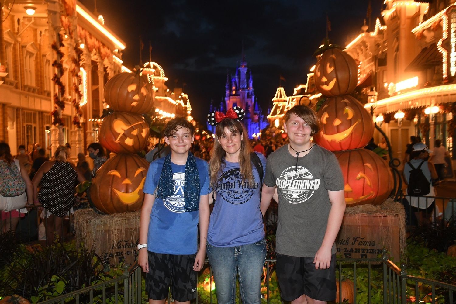 Nighttime view of Main Street USA at Disney World with illuminated pumpkins and castle visible in background.