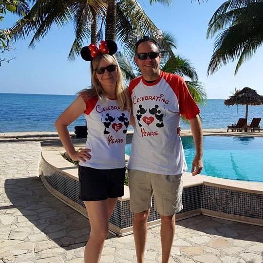 Couple in matching Disney cruise vacation shirts posing by a tropical resort pool.