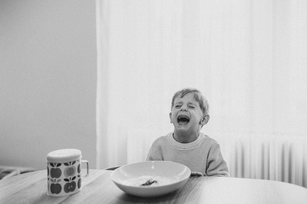 Joyful moment captured in black and white as child laughs at dining table with plate and mug.