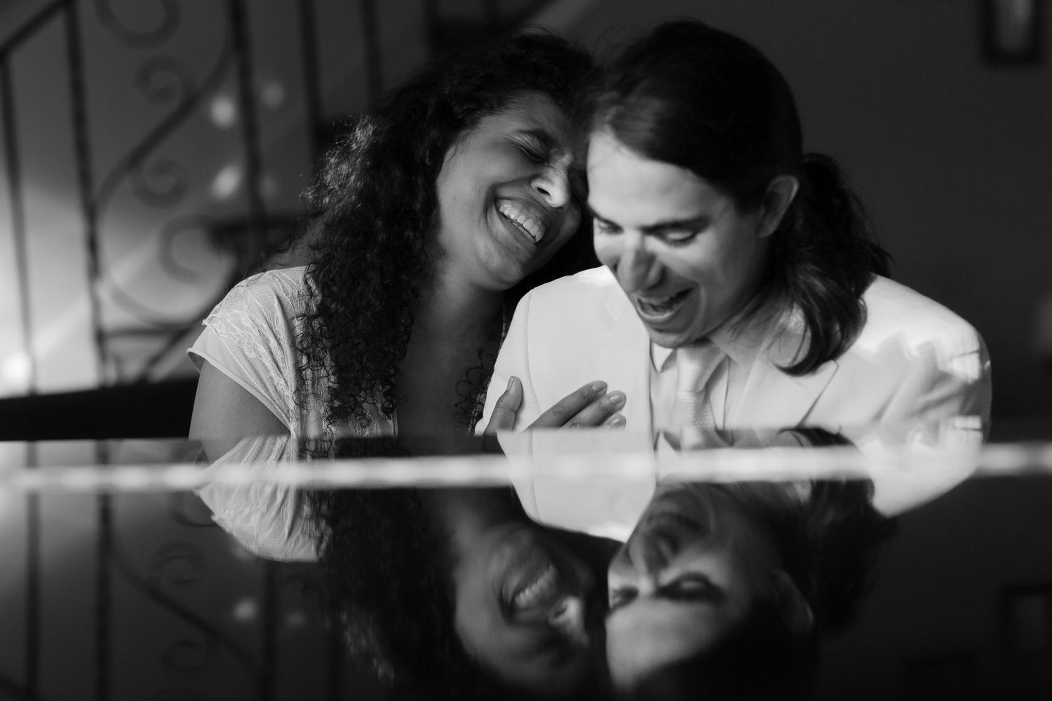 A black and white photo of a smiling couple leaning together over a reflective glass table surface.