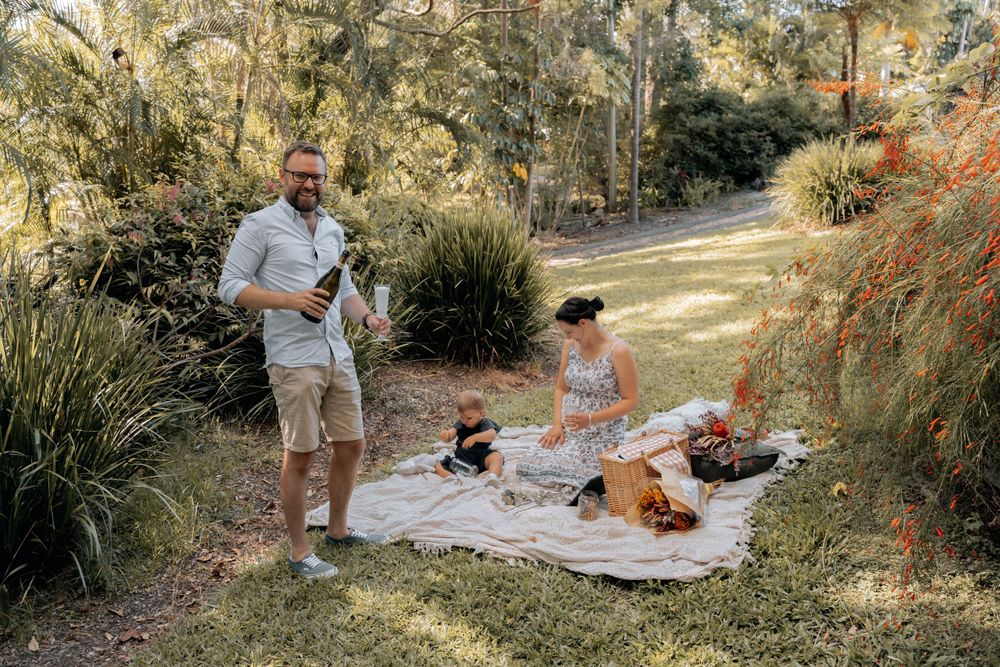 A relaxed outdoor picnic scene with a blanket spread on grass surrounded by ornamental plants.