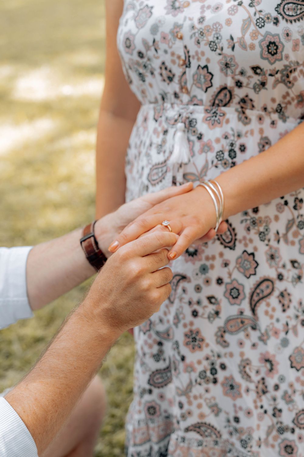 Close-up of hands placing an engagement ring on a finger, with a paisley patterned dress in view.