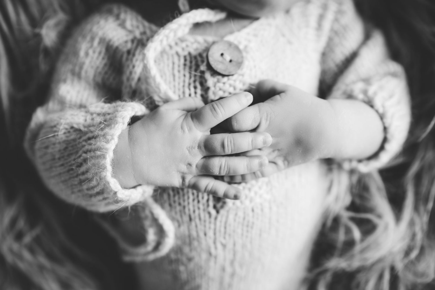 Black and white close-up of baby hands holding knitted sweater.