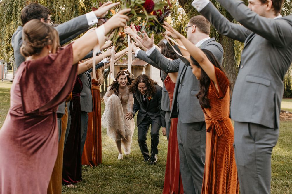 Bride and groom walk through tunnel of raised hands formed by wedding party outdoors.