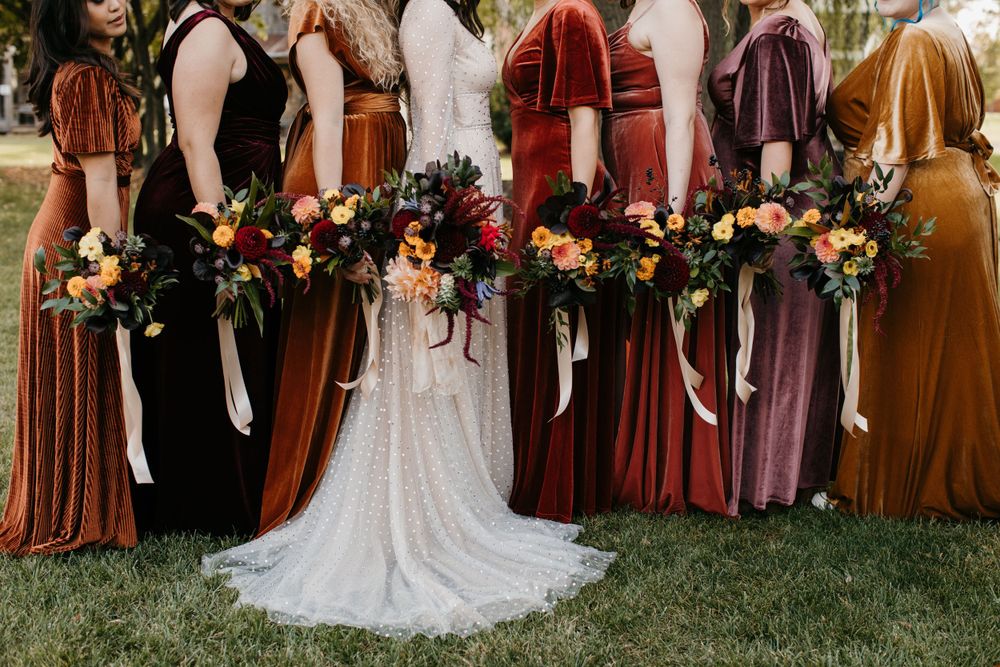 Close-up of bride in beaded gown surrounded by bridesmaids holding lush fall floral bouquets.
