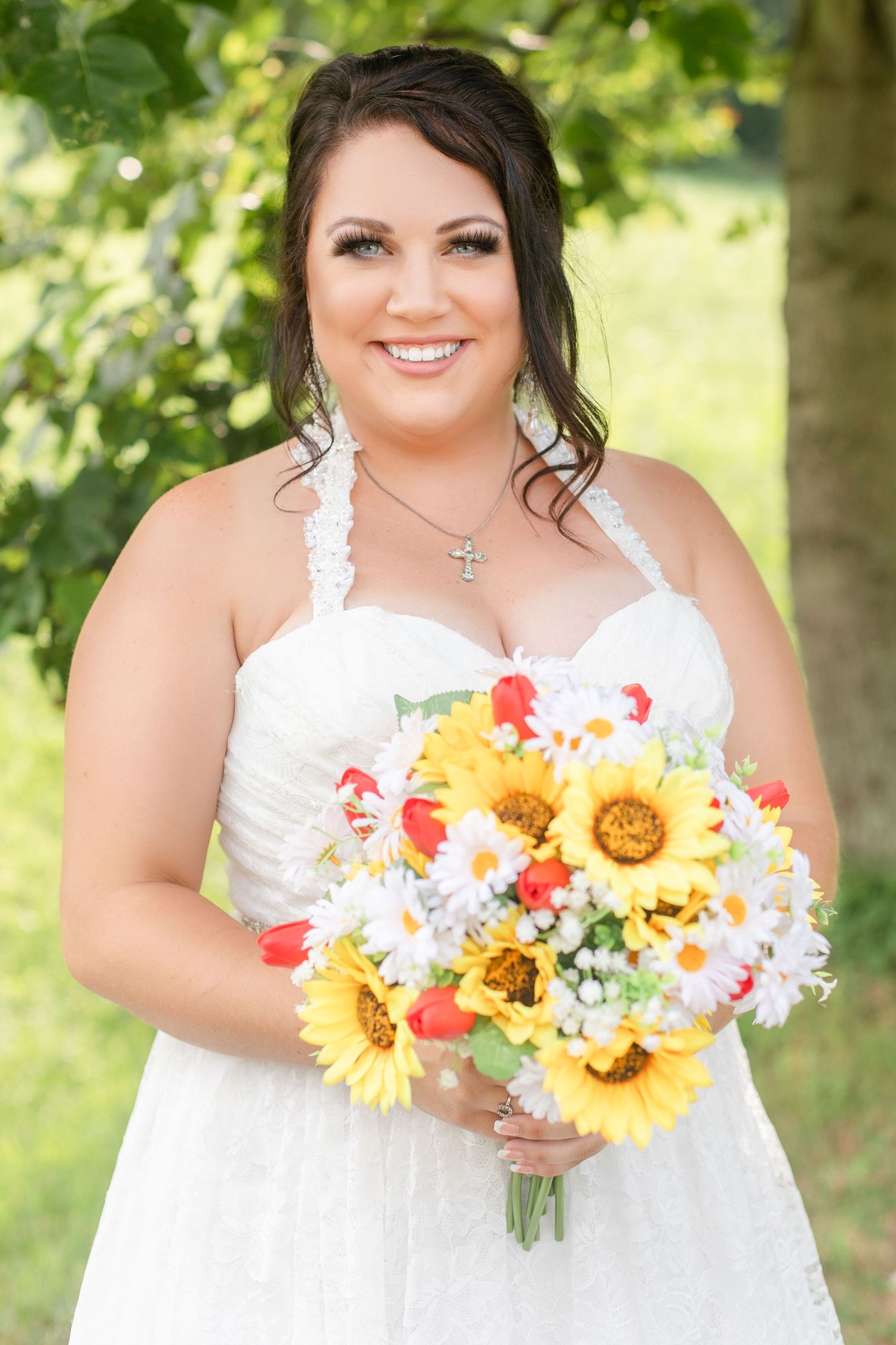 Bride with summer bouquet featuring sunflowers and daisies against green foliage.