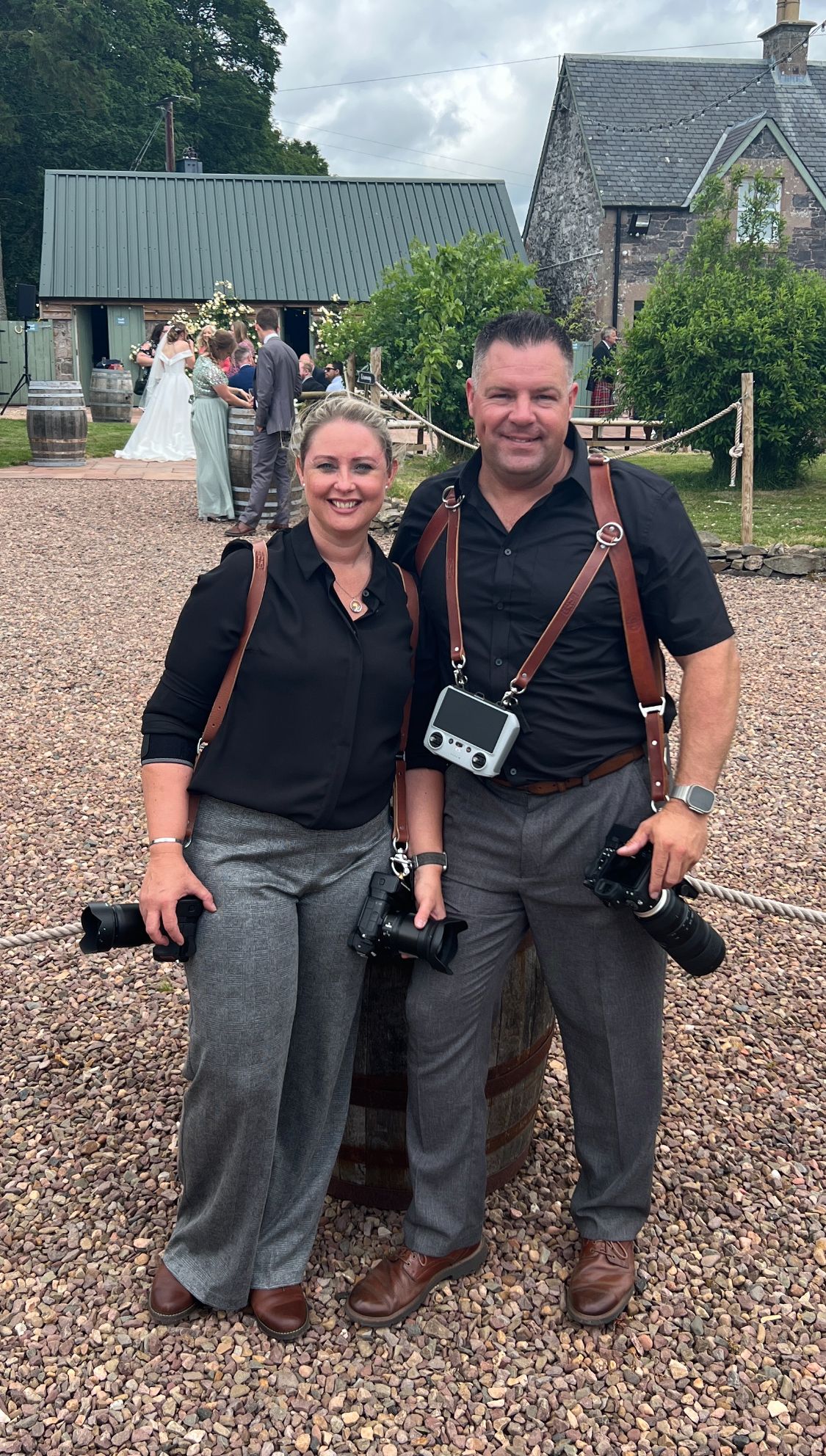 Two photographers with professional cameras and gear standing on gravel path at wedding venue.