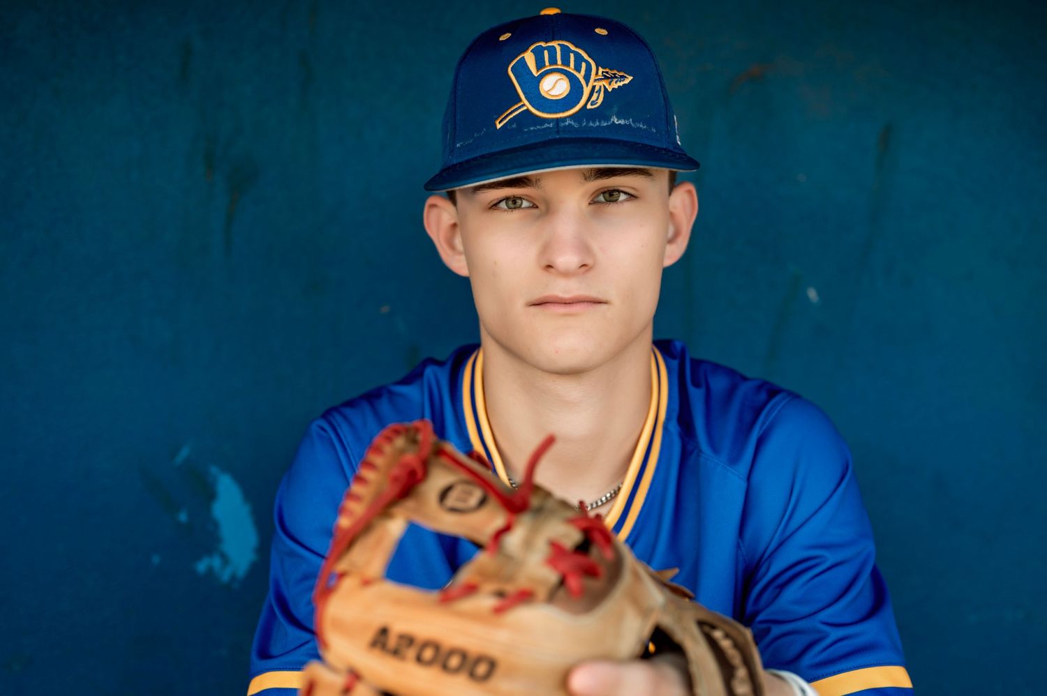 Baseball player in blue uniform sitting in dugout with glove.