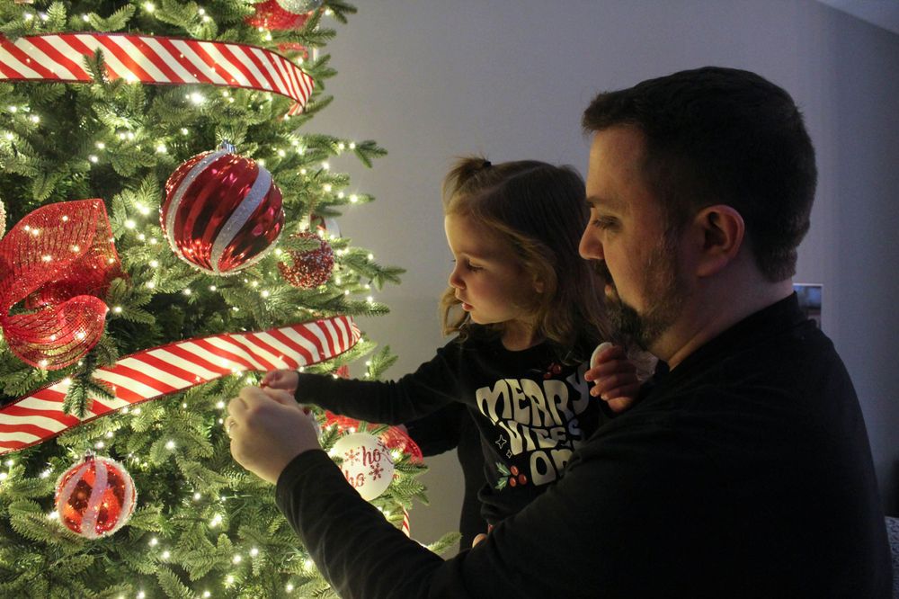 Parent and child hanging ornaments on illuminated Christmas tree with candy cane decorations.