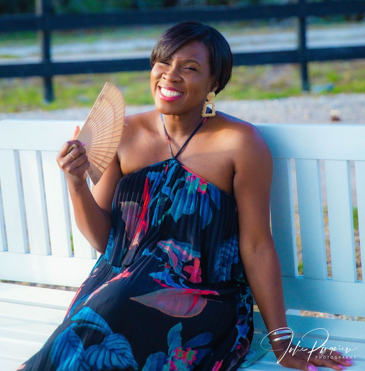 A summer portrait on a white bench with decorative hand fan and floral dress.