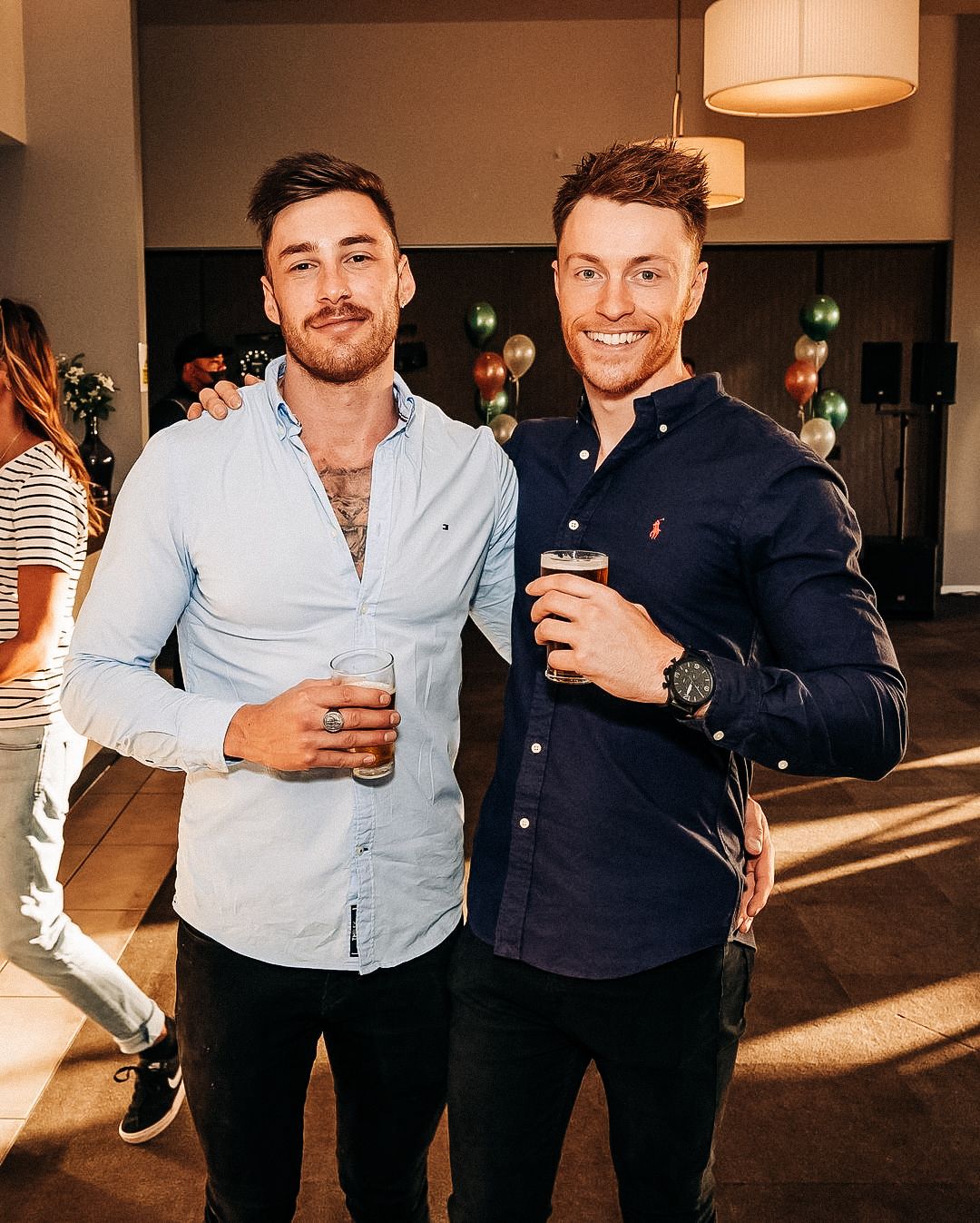 Two people enjoying drinks at an indoor social gathering with ambient lighting.