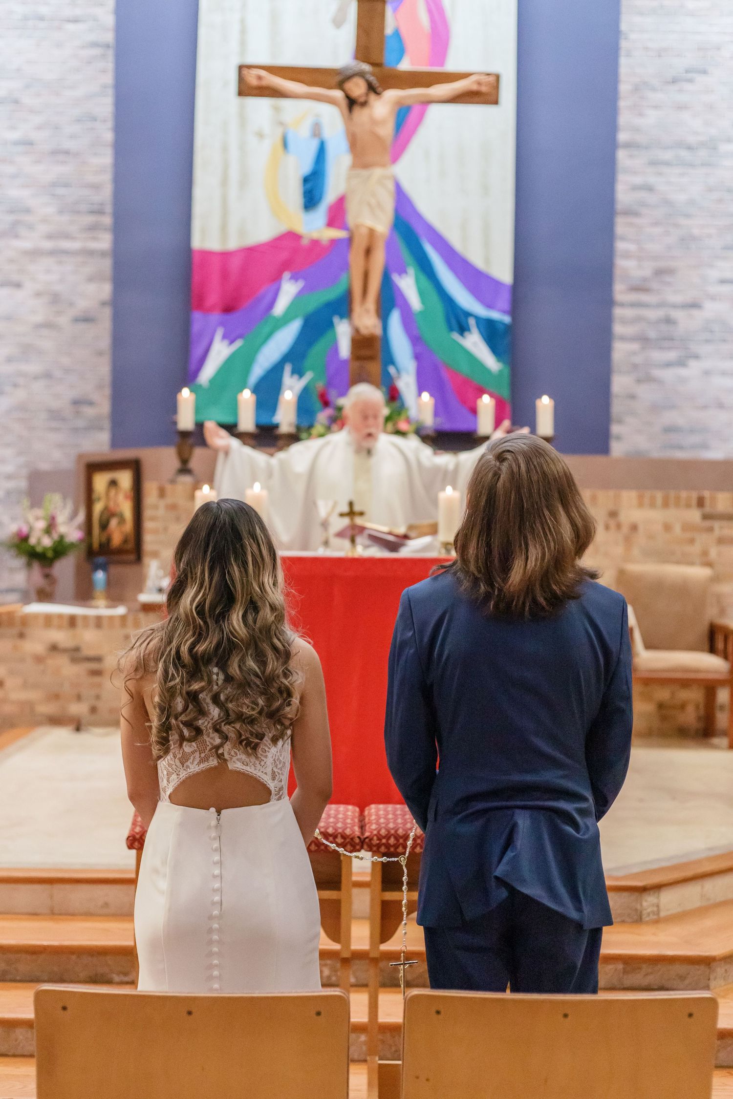 Couple stands before colorful church altar during wedding ceremony.