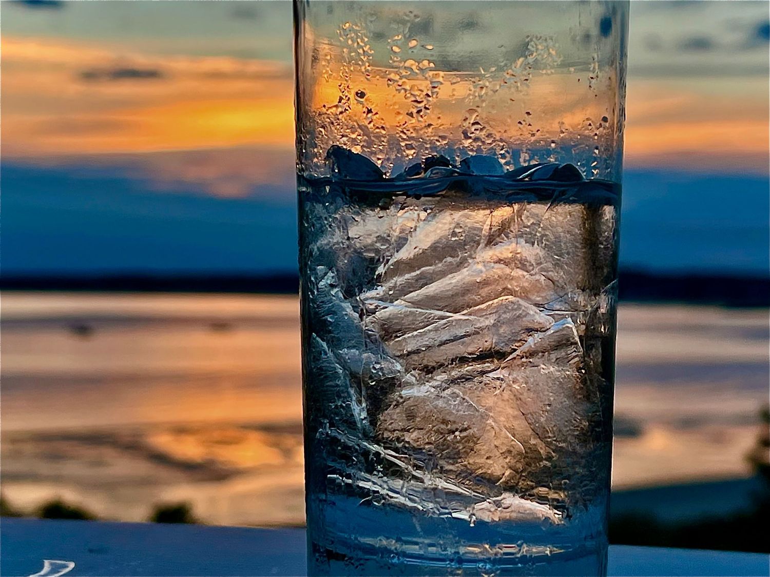Closeup of ice cubes in glass with golden sunset reflecting through.