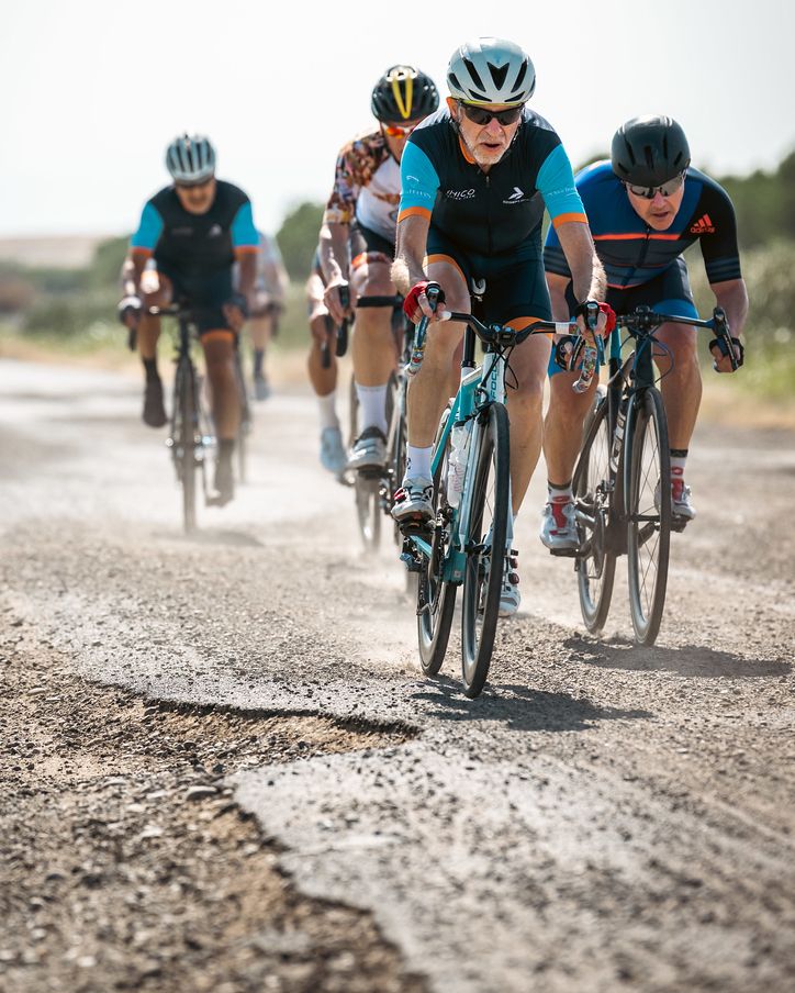 Group of cyclists racing on a gravel road wearing cycling gear and helmets.