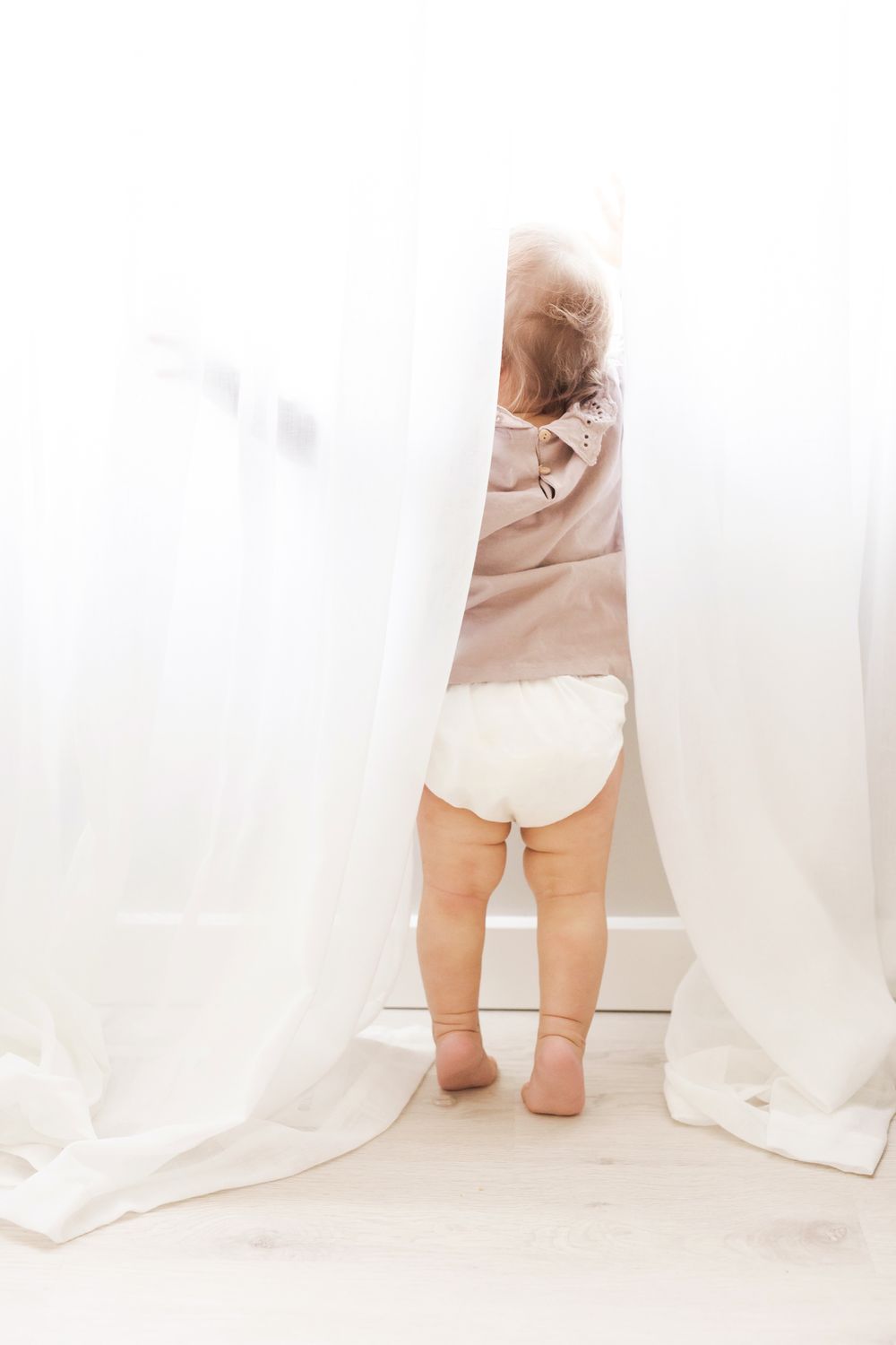 baby girl looking out window with sheer curtains light and airy