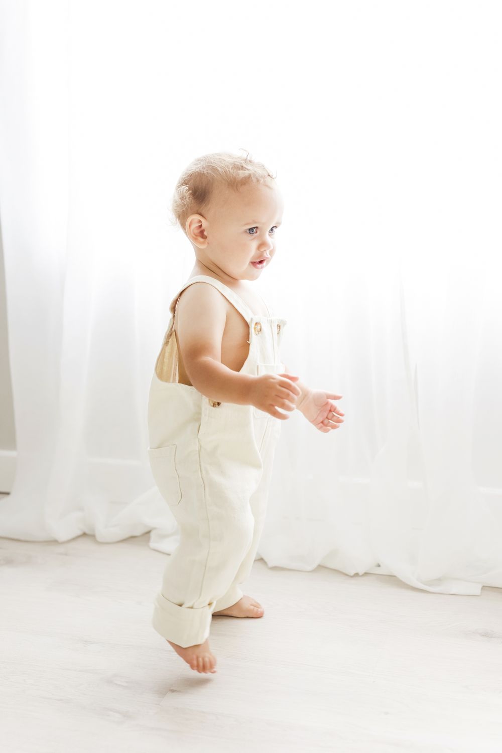 one year baby boy walking in front of window sheer curtains backlit light and airy