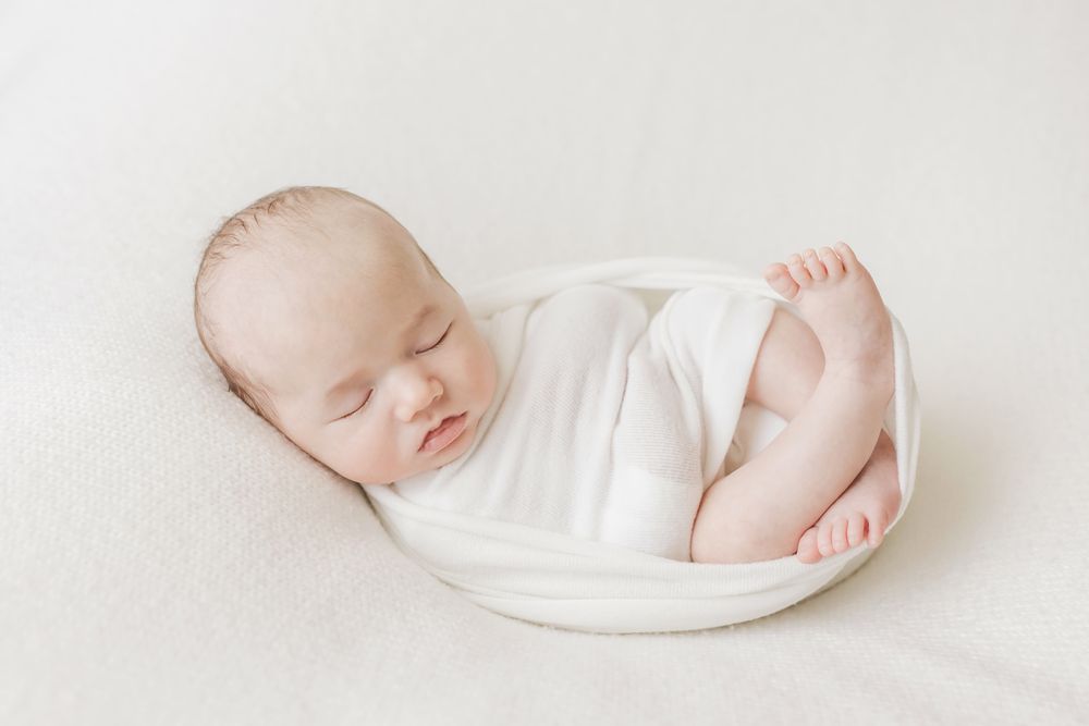 newborn baby wrapped with toes showing on bean bag with light colored fabric