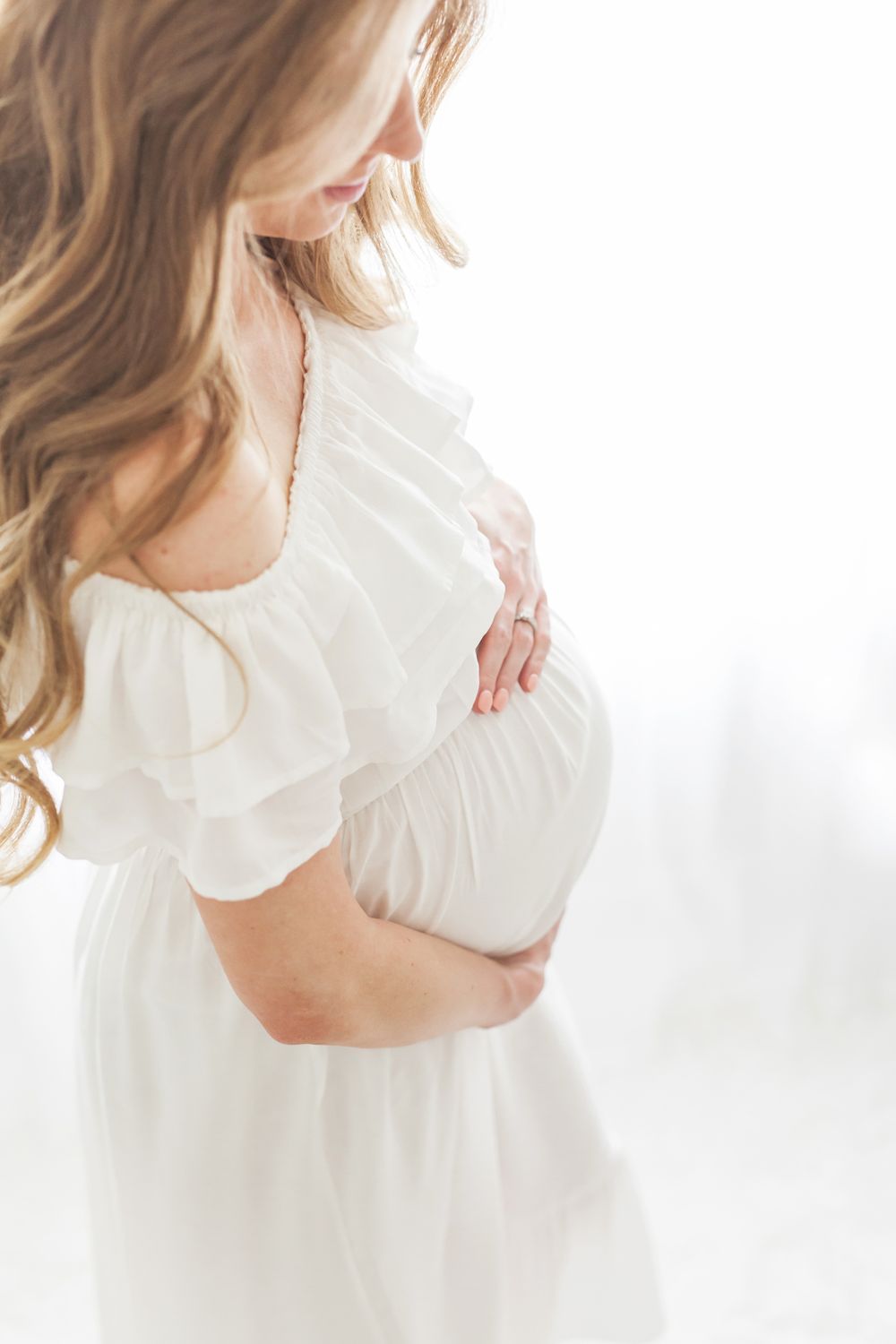mother holding pregnant belly white dress backlit light and airy