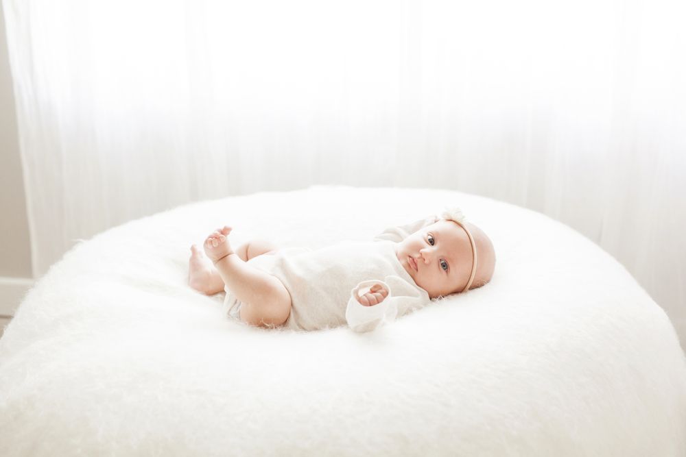 baby girl on bean bag in front of window backlit light and airy