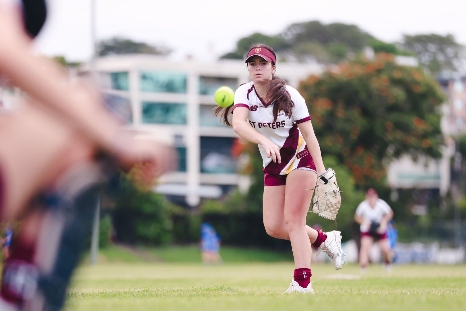 Softball player in maroon uniform leaps to make a throw during game.