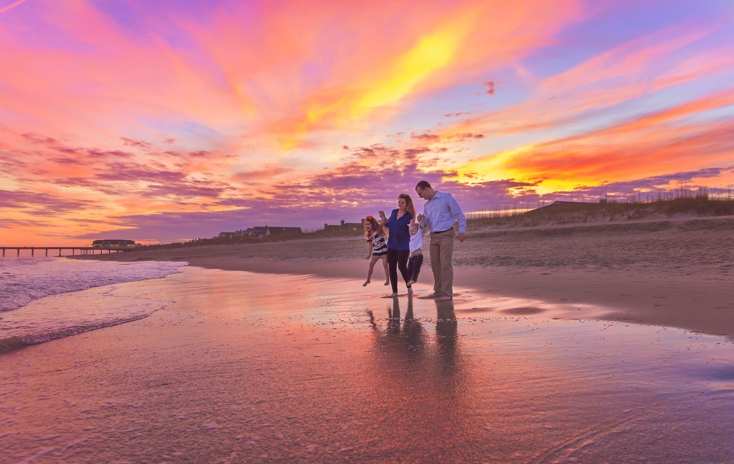 Silhouettes of people walking on beach during dramatic colorful sunset.