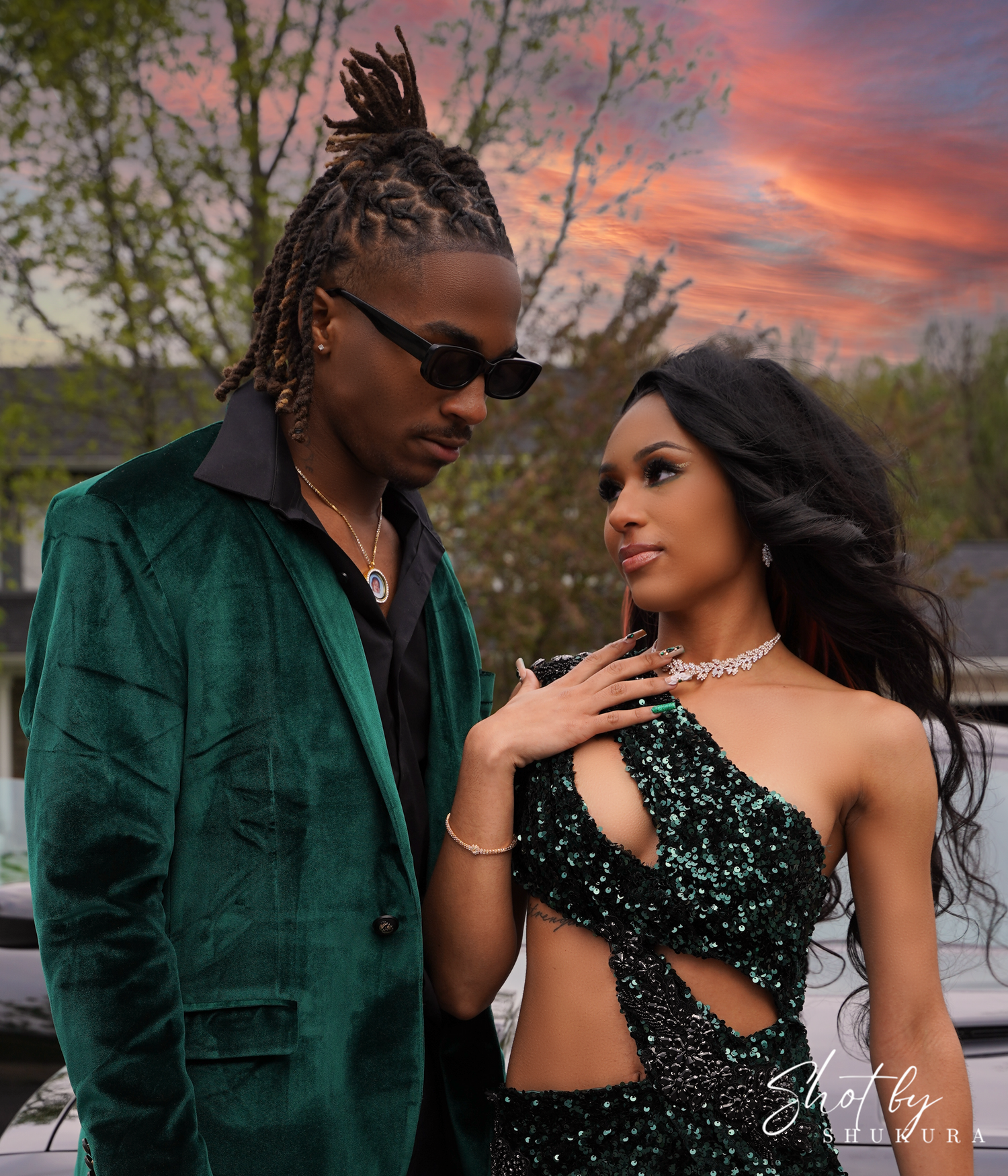 Glamorous couple in evening wear poses against a sunset sky.