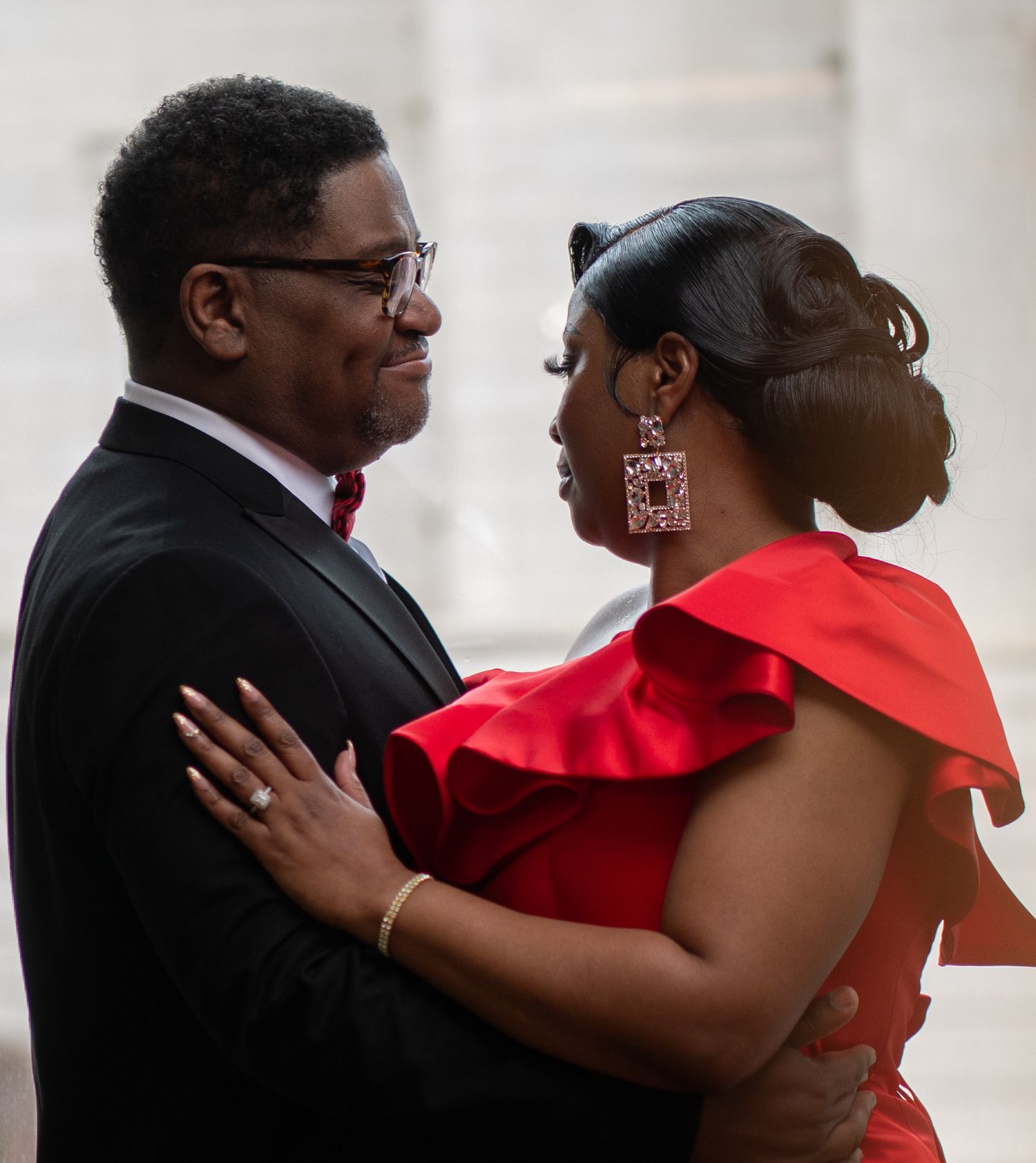 A couple shares an intimate moment wearing formal attire with a red dress and black tuxedo.