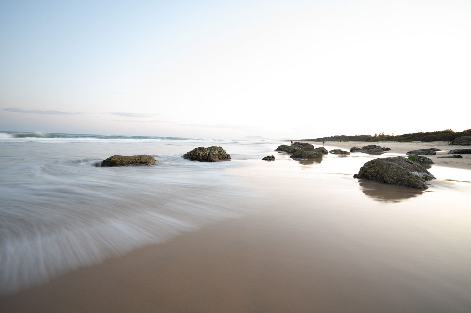 Long exposure seascape of rocky beach at sunrise with smooth water motion.