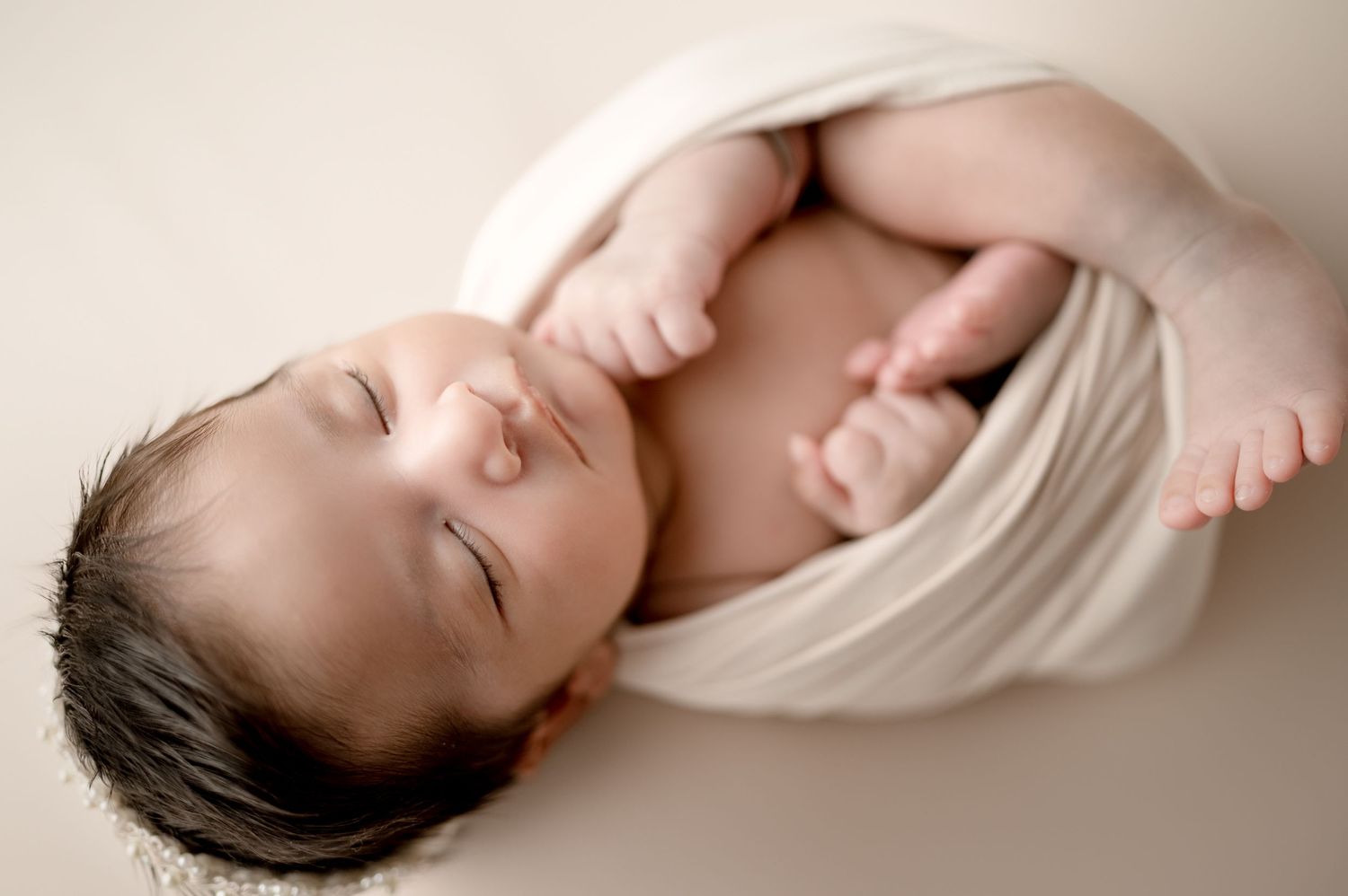 Peaceful sleeping newborn wrapped in white fabric against neutral backdrop.