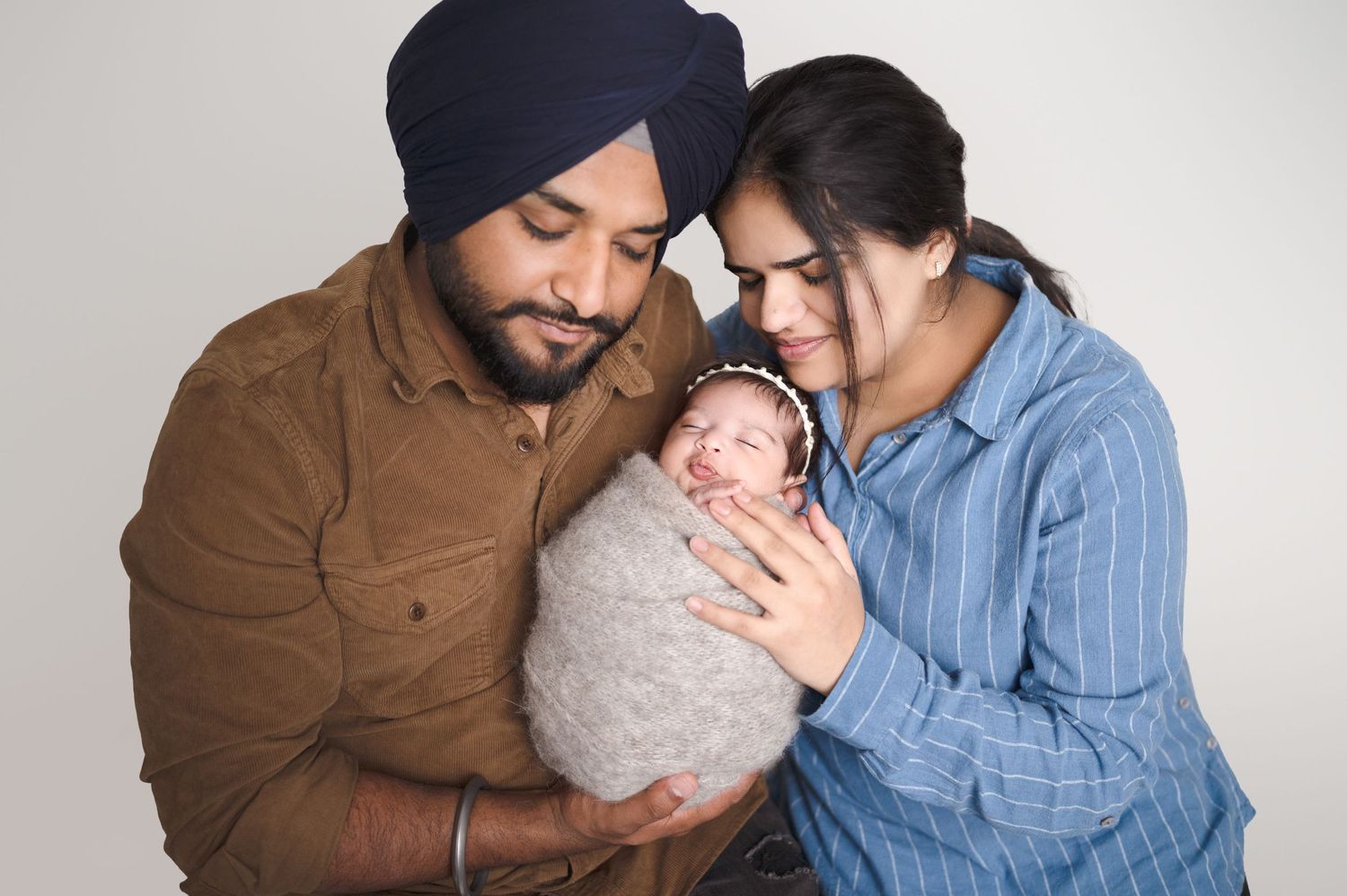 Parents in casual attire tenderly holding their swaddled newborn during studio photoshoot.