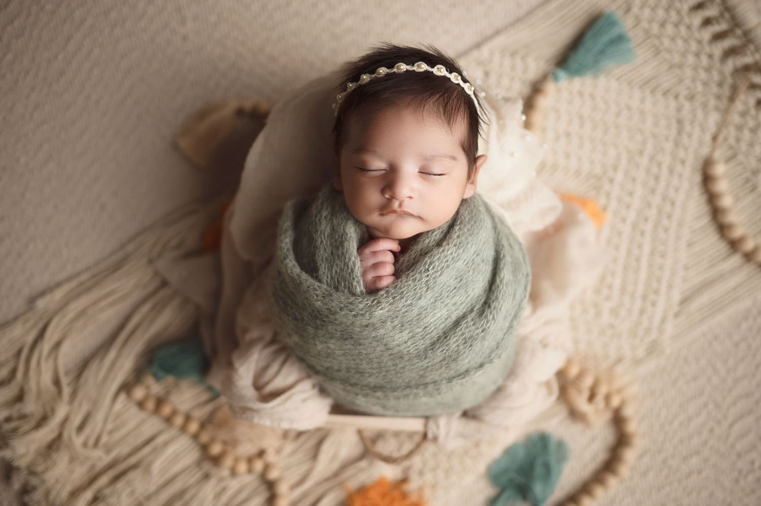 Sleeping newborn in sage wrap with headband on textured knit blanket.