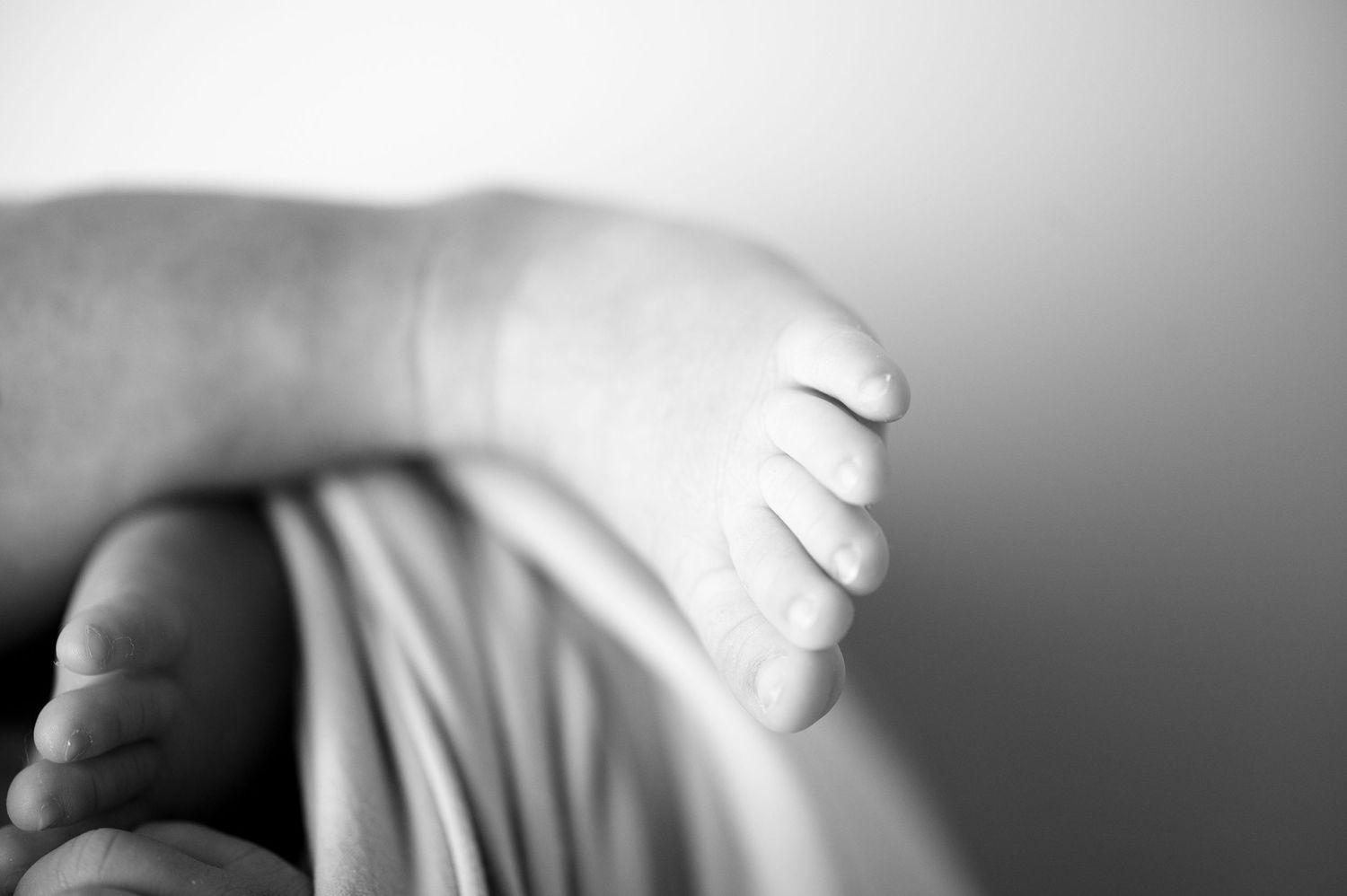 Black and white detail shot of tiny newborn foot wrapped in fabric.