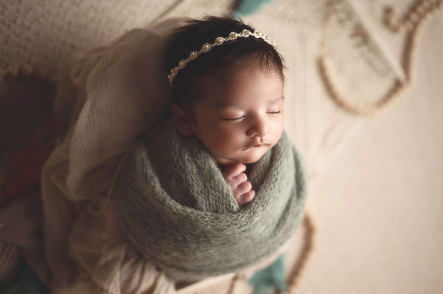 Overhead view of newborn in green wrap sleeping on textured cream blanket.